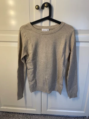 Beige stickad tröja från Vila - En enkel och stilren beige stickad tröja från Vila. Tröjan har rund halsringning, långa ärmar och ribbade muddar vid ärmslut och nederkant. Perfekt basplagg i mjukt material som passar till det mesta.