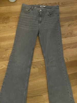 Gråa bootcut jeans från NA-KD - Säljer ett par gråa jeans från NA-KD med klassisk femficksdesign och vida ben. Jeansen har normal passform och är tillverkade i ett mjukt bomullsjeansmaterial. Perfekta för en avslappnad och stilren look. Endast använda få gånger och köpta för 350kr. Kan sänka priset!!