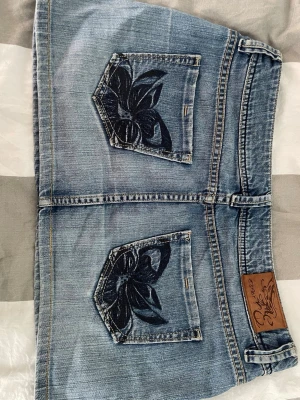 Blå jeanskjol med broderade fickor - Säljer denna fina jeanskjolen med jättesnygga broderade fickor. Jag skulle säga att storleken är ungefär M. Midjemåttet är ca 45cm och ungefär 30 cm lång. Skriv om du har funderingar, pris går att diskuteras🩷