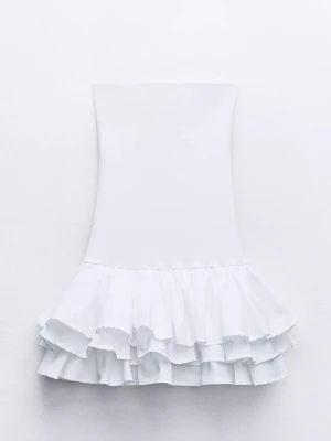 Vit axelbandslös volangklänning - Säljer en vit axelbandslös kortklänning med flera lager volanger nedtill. Klänningen har en figurnära passform upptill och en fluffig kjol med volangdetaljer som ger en lekfull look. Perfekt för sommarens alla tillfällen!