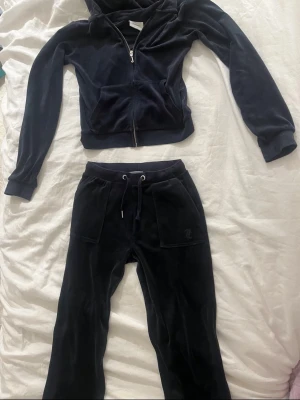 Mörk blått juicy counture sett - Mysigt svart loungewear-set i mjuk velour med zip-hoodie och matchande byxor. Hoodien har dragkedja och fickor framtill, byxorna har dragsko i midjan och två stora fickor. Perfekt för chill dagar hemma. Diskret broderad logga på byxan. Kommer aldrig till användning längre, tröjan har lite fläckar vid armarna! 