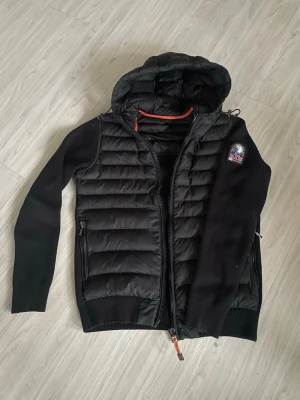 Parajumpers jacka - NYPRIS: 3995kr                                                                                    Snygg svart pufferjacka från Parajumpers med vadderad front och huva. Jackan har stickade ärmar och muddar, dragkedja framtill och två sidofickor med dragkedja. Märkets patch sitter på vänster ärm. Perfekt för kalla vinterdagar.