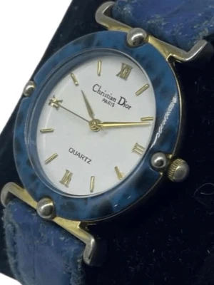 Blå vintageklocka 1980-tal från Christian Dior - Snygg blå klocka från Christian Dior med rund urtavla, guldfärgade detaljer och romerska siffror. Klockan har ett blått armband och en vit urtavla med quartz-urverk. Perfekt accessoar för dig som vill ha något unikt och stilrent.