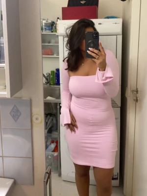 Ljusrosa långärmad kortklänning - Säljer en ljusrosa, figurnära kortklänning med långa ärmar och slits i ärmslut. Klänningen har en fyrkantig urringning och är tillverkad i ett stretchigt material som framhäver siluetten. Perfekt för dig som gillar en feminin och trendig look.