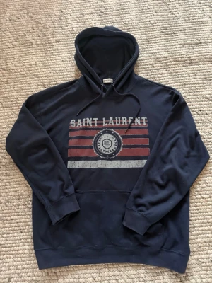  Saint Laurent hoodie - Säljer denna super eftertraktade och exklusiva hoodie från Saint Laurent. Perfekt för dig som gillar en bakåtlutad stil med klass. Storlek L. Använd sparsamt 😁pris ej hugget i sten, hör av er om ni har någon fråga!
