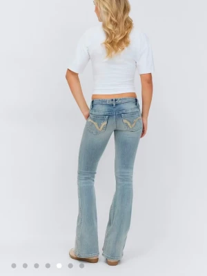 Ljusblå bootcut jeans från Gina Tricot - Ljusblå bootcut jeans från Gina Tricot med slitningar på framsidan och snygga broderade detaljer på bakfickorna. Jeansen har låg midja och klassisk femficksdesign. Perfekt för dig som gillar en avslappnad och trendig look.