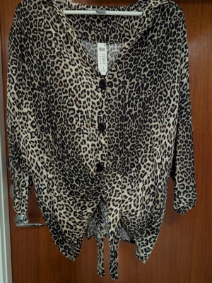 Leopardmönstrad blus med knyt - Snygg leopardmönstrad blus från Lindex med trekvartsärm och knappar framtill. Blusen har ett knytband nedtill.