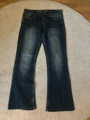 Mörkblå bootcut jeans Gazoz - Snygga mörkblå bootcut jeans från Gazoz med slitningar framtill och broderade bakfickor. Klassisk femficksmodell med låg midja och utsvängda ben. Perfekta för dig som gillar en retro vibe och vill sticka ut lite extra.