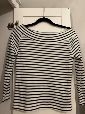 Randig offshoulder topp i bomull - Säljer en vit och svart randig offshoulder topp med lång ärm. Toppen har en bred urringning som sitter snyggt över axlarna och är gjord i mjuk bomull. Perfekt för en chill och stilren look. ⭐️Toppen är i storlek L men passar XS🩷
