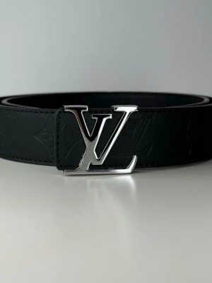 Svart bälte med silver logga - Snyggt svart skärp i skinn med klassisk silver logga. Bältet har diskret präglat monogrammönster längs hela bandet och känns riktigt lyxigt och stilrent. Perfekt accessoar för att lyfta vilken outfit som helst.