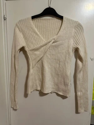Beige ribbad omlottopp strl: L men är mer som S - Säljer en beige stickad omlottopp med ribbad struktur och lång ärm. Tröjan har en djup V-ringning och sitter figurnära. Perfekt att styla med jeans eller kjol för en trendig look. Ev lös tråd. 