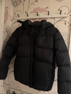 Svart pufferjacka från Tommy Hilfiger - Snygg svart pufferjacka från Tommy Hilfiger med huva och diskret logga på bröstet. Jackan har en klassisk quiltad design, dragkedja framtill och två sidofickor. Perfekt för kalla dagar när du vill hålla värmen och ändå se stilren ut.💗Nypris är ungefär 1500 så lägger upp den för 950 då den är som helt ny, men kom gärna med egna prisförslag!