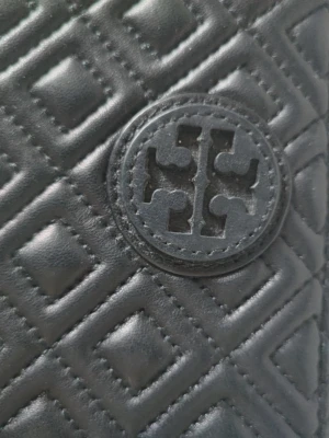 Svart quiltad plånbok från Tory Burch - Stilren svart plånbok från Tory Burch med quiltat mönster och det ikoniska logotyp-emblemet på framsidan. Plånboken är tillverkad i läder och har en kompakt, fyrkantig form som är perfekt för att organisera kort och kontanter.