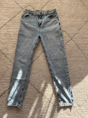 Ljusblå jeans från Lindex - Säljer ett par ljusblå jeans från Lindex med klassisk femficksmodell och hög midja. Jeansen har raka ben och bälteshällor, tillverkade i denim med en snygg tvättad look. Perfekta för en avslappnad och trendig stil. Det är ett skönt material och jeansen är i ett bra skick!