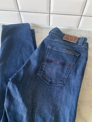 Nudie Jeans  - Säljer ett par superfina Nudie Jeans i modellen Lean Dean. Färgen heter Deep Sparkle och är en riktigt snygg, djup mörkblå tvätt med lätta slitningar som ger dem en schysst karaktär. Lean Dean är en av Nudies populäraste passformer – en klassisk slim fit med smala ben som smalnar av hela vägen ner till fotleden. Detaljer: • Modell: Lean Dean • Tvätt: Deep Sparkle (Mörkblå) • Storlek: W30 / L32 • Material: 98% ekologisk bomull, 2% elastan (skön stretch!) • Skick: Mycket bra begagnat skick. Väl om