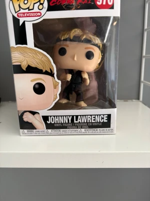 Johnny Lawrence Funko Pop figur - Cool samlarfigur av Johnny Lawrence från Cobra Kai, modell 970. Figuren är gjord i vinyl och har blont hår, svart pannband och svart dräkt. Perfekt för dig som gillar TV-serier och popkultur.