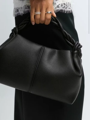 Svart handväska med tvinnat handtag - Stilren svart handväska i slätt konstläder med ett unikt tvinnat handtag. Väskan har en mjuk, rundad form och minimalistisk design utan synliga loggor. Perfekt för dig som gillar en clean look med en twist.