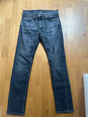 Lean Dean jeans från Nudie jeans  - Snygga svarta jeans från Nudie jeans med slim passform och klassisk femficksdesign. Jeansen har en lätt tvättad look och är tillverkade i slitstark denim. Perfekta för dig som gillar en trendig stil. Storleken är 30W/32L och modellen är Lean Dean