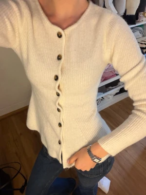 Vit ribbstickad kofta med knappar - Snygg vit ribbstickad kofta med svarta knappar, perfekt att slänga över en t shirt eller topp🫶🏽 helt ny utan prislapp!💕💕