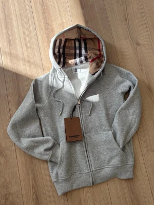 GRÅ BURBERRY HOODIE (S) JUNIOR - Säljer en grå burberry hoodie för endast 499kr(fastpris) har aldrig använt den och är i perfekt skick. Storlek X/XS för junior