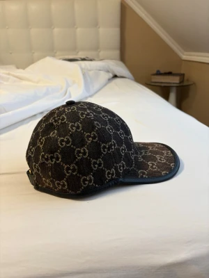  Gucci keps svart denim, LIMITED EDITION - Säljer en snygg Gucci keps i svart denim med det klassiska GG-mönstret över hela kepsen. Justerbar rem bak i svart läder med guldfärgad spänne. Perfekt accessoar för dig som vill ha en exklusiv och trendig look. Present av frugan i Paris, digitalt kvitto finns. LIMITED EDITION 