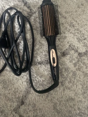 Xenia Mini Comb värmeborste - Xenia Mini Comb är en elektrisk värmeborste i svart med detaljer i guld. Den har rund form med täta borst och lång sladd för enkel styling. Borsten är tillverkad i plast och metall och kommer med en svart quiltad förvaringsväska samt originalförpackning.