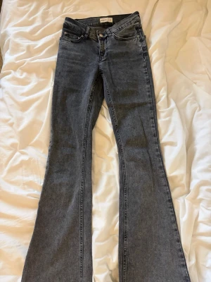 Grå bootcut jeans från Gina Tricot - Säljer ett par grå bootcut jeans från Gina Tricot med klassisk femficksdesign och knappgylf. Jeansen har en snygg tvättad look och är tillverkade i denim med stretch för skön passform. Perfekt för dig som gillar trendiga siluetter.