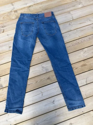 Blå jeans med raka ben - Säljer ett par klassiska blå jeans med raka ben och två bakfickor. Jeansen har en snygg mörkblå ton och är tillverkade i bomull. Perfekta för dig som gillar en enkel och tidlös stil.