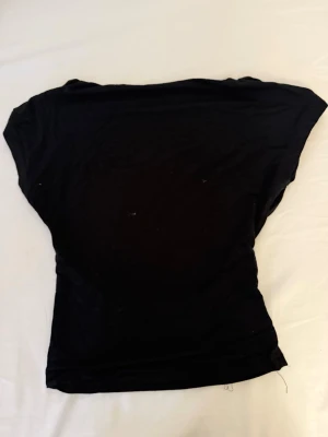 Svart kortärmad topp - En enkel svart topp med korta ärmar och rund hals. Modellen är figurnära och passar perfekt till jeans eller kjol. Toppen är rygglös