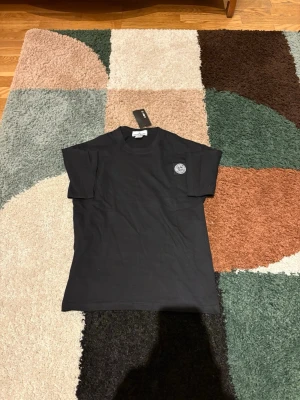 Svart t-shirt från Stone Island - Påse ingår! Säljer en snygg svart t-shirt från Stone Island med klassisk logopatch på bröstet. T-shirten är helt oanvänd med prislapp och passar perfekt till sommaren! Den är i storlek M men passar även som S. Skriv vid funderingar, mvh Andreas!                                                                 