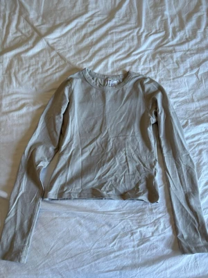 Beige långärmad topp  - En enkel och stilren beige långärmad topp. Modellen är croppad med rund halsringning och har en slim passform. Perfekt att matcha med jeans eller kjol för en clean look.
