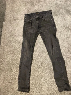 Svarta slim jeans från Nudie Jeans - Säljer ett par svarta skinny jeans från Nudie Jeans med klassisk femficksmodell och dragkedja. Jeansen har en tvättad look och är tillverkade i stretchigt denimtyg för skön passform. Perfekta till en avslappnad stil.