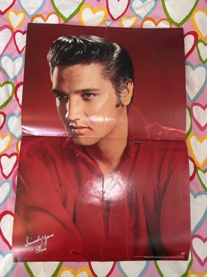 Röd Elvis Presley affisch - Affisch med Elvis Presley i röd skjorta mot röd bakgrund. Tryckt signatur 'Sincerely Yours Elvis' i vitt nere till vänster. Den har vikmärken som säkert blir bättre om man bara lägger den lite i press men annars superfint skick. I högra hörnet står det ”Distributed in the UK by BMG Records” men vet inte var den är ifrån. Perfekt för dig som gillar musiknostalgi och vill ha något unikt på väggen. Pris kan diskuteras!