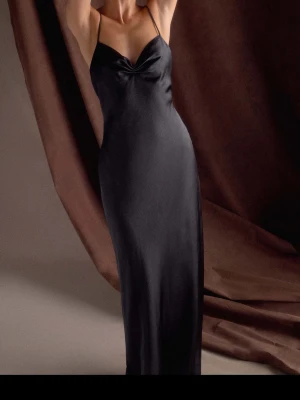 Svart långklänning med tunna band - Elegant svart långklänning med smala axelband och lätt v-ringad urringning. Klänningen har en figurnära passform och är tillverkad i ett glansigt, mjukt material som ger en lyxig känsla. Perfekt för dig som vill ha en stilren och tidlös look. Från meshki bara testad en gång! Den är i M men passar mig som har S.