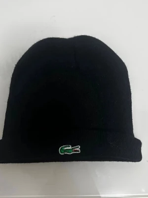 Svart mössa från Lacoste - Svart ribbstickad mössa perfekt för dig som vill ha en stilren och ikonisk accessoar.