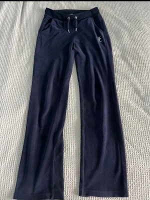 Mörkblå Juicy Couture mjukisbyxor - Mörkblå mjukisbyxor från Juicy Couture med raka ben, dragsko i midjan och fickor. Klassisk Juicy-logga i strass på baksidan. Mjukt och skönt material, perfekt för en chill look. I storlek xs men tycker att de är större typ som en s eller m.