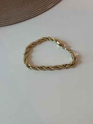 Tjockt tvinnat guldarmband - Snyggt armband i guldfärgad metall med tvinnad kedja och karbinlås. Armbandet har en chunky känsla och passar perfekt för dig som gillar statement-smycken. Enkel att matcha med andra accessoarer och ger en lyxig touch till din stil.