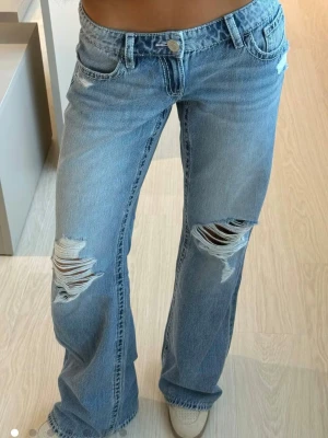 Low waist loose jeans - Säljer ett par ljusblå low waist loose jeans med slitningar och hål på knäna. Jeansen har klassisk femficksdesign, knappstängning och är tillverkade i denim. Perfekt för dig som gillar en avslappnad och trendig look. De är inköpta för 430kr och i bra skick. Använda och tvättade få gånger 