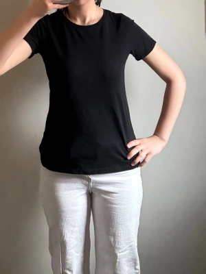 Svart basic t-shirt i bomull - En enkel svart t-shirt med rund hals och korta ärmar. Modellen är klassisk och passar perfekt till jeans eller shorts. Materialet är mjukt och skönt bomull som känns bekvämt mot huden. Perfekt för dig som gillar en clean och stilren look.