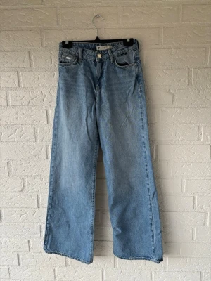 Blå wide leg jeans från Mavi - Säljer ett par ljusblå wide leg jeans från Mavi med klassisk femficksdesign och hög midja. Jeansen är tillverkade i denim och har en avslappnad passform som ger en cool och trendig look. Perfekta för dig som gillar en loose fit och retrostil. Midja 35-36cm x2 ca 70-72 cm  Längd 103cm Innerbensmått 75cm 