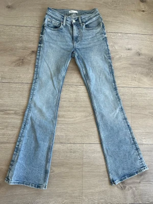 Blå bootcut jeans från Gina Tricot - Säljer ett par ljusblå bootcut jeans från Gina Tricot med klassisk femficksdesign och snyggt läderpatch bak. Jeansen har en lätt tvättad look och är tillverkade i bomull. Perfekta för dig som gillar en avslappnad och trendig stil. De har bara används någon enstaka gång, nyskick! Priset går att diskutera!