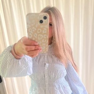 Randig smock- blus från Gina Tricot - Supersöt blus från Gina Tricot i storlek S. Den är vit med tunna blå ränder, har smockdetaljer över bröst och rygg, samt puffiga långärmar. Knäppning framtill med små vita knappar. Perfekt för dig som gillar en fräsch och chill stil.