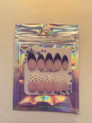 Press-on naglar svart och vit prickig - Handgjorda press-on naglar i mandelform med svarta och vita polkadots. Basen är nude och designen är trendig och lekfull. Perfekt för dig som vill ha en cool och unik nagelstil utan att behöva gå till salong. Kommer i förpackning med 10 naglar i storlek S.