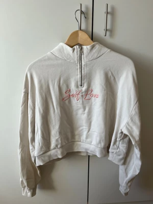 Vit hoodie med halv dragkedja - Vit hoodie med halv dragkedja framtill och broderad text 'Self Love' i rosa på bröstet. Tröjan har en croppad passform och är från H&M💕💕
