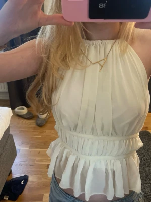 Ljus-gul omlott halterneck blus med volang - Säljer en ljus-gul halterneck blus med omlott och volangdetaljer. Toppen har öppen rygg och knytband både i nacken och runt midjan. Materialet är lätt och luftigt, perfekt för varma dagar. Passformen är normal och toppen är ärmlös.