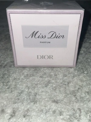 Miss Dior Parfum från Dior - Helt ny med plaster på. Miss Dior Parfum från Dior i en elegant ljusrosa kartong med silverdetaljer. Klassisk och lyxig design, perfekt för dig som vill ha en ikonisk doft från ett välkänt märke. Förpackningen är tillverkad i kartong och parfymen är producerad i Frankrike.