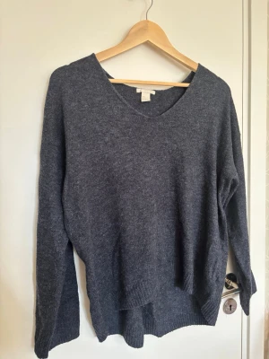 Mörkgrå stickad tröja med v-ringning - Säljer en mörkgrå stickad tröja från H&M med v-ringning och långa ärmar. Tröjan har en avslappnad passform och ribbstickade muddar vid ärmslut och nederkant. Perfekt för lager-på-lager och enkel att matcha med jeans eller kjol.