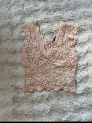 Rosa spets topp från Zara - Supersöt rosa spets topp från Zara med v-ringning och breda axelband. Toppen är ärmlös och har fina volangdetaljer längs kanterna. 