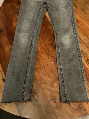 Grå  jeans från Nudie Jeans - Säljer ett par gråa jeans från Nudie Jeans. Jeansen har klassiska bakfickor med Nudie Jeans signaturbrodyr och bälteshällor. Perfekta för en avslappnad och trendig look. Slim fit w30 l 26