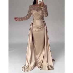Champagnefärgad långklänning LanTing - Säljer en elegant champagnefärgad långklänning från LanTing med glittrig överdel täckt av paljetter och långärmade ärmar. Kjolen är i mjuk satin med vacker drapering och markerad midja. Perfekt för dig som vill sticka ut med lyxig stil och glans.
